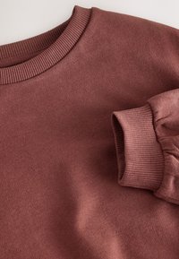 Pull doux mauve à manches longues avec col rond côtelé et poignets côtelés, présenté plié sur un fond clair.