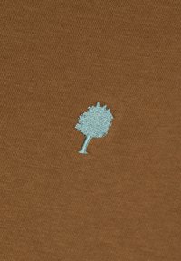 Piccolo albero ricamato blu chiaro su sfondo di tessuto texturizzato marrone, centrato nella cornice.