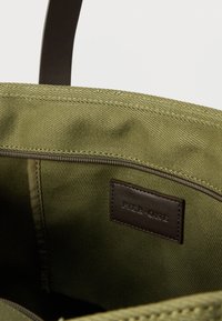 Εσωτερικό από υφασμάτινη τσάντα tote ελιάς, με δερμάτινη ετικέτα που γράφει "PIER ONE." Με ομαλή υφή, κλείσιμο με φερμουάρ και ραφές λεπτομερειών.