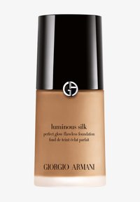 Lasipullo, jossa on beige sävy. Varustettu mustalla korkilla, jossa on logo ja teksti "luminous silk perfect glow flawless foundation."