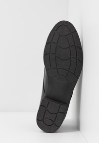 Semelle de chaussure noire en caoutchouc texturé, avec un design de grip en relief. Taille 37 imprimée sur le côté. Forme plate et large.