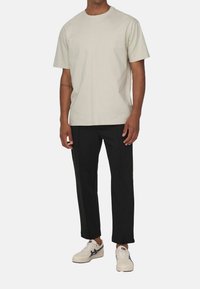 Hellgraues T-Shirt mit kurzen Ärmeln und Rundhalsausschnitt, kombiniert mit schwarzen geraden Hosen und weißen Sneakers mit blauen Akzenten.