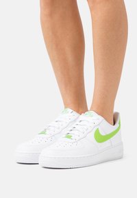 Vita lädersneakers med en grön Nike-logotyp, perforerat tåparti och matchande gröna detaljer på tungan. Platt gummisula för bra grepp.