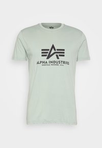 Lys grøn bomulds t-shirt med kortærmer, fremhævende en sort grafik af "ALPHA INDUSTRIES" og logo på forsiden. Rund halsudskæring.