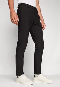 Sorte slim-fit bukser lavet af strækstof, med sidelommer, lynlås og en subtil tekstureret finish, parret med hvide sneakers.