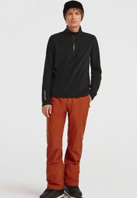 Sort zip-hals langærmet top, orange skibukser, sort hue og sorte sko. Glat stof, tætsiddende design og holdbare detaljer.