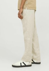 Lichtbeige linnen broek met een rechte snit, voorzien van een subtiele textuur. Gecombineerd met crèmekleurige sneakers met zwarte strepen.
