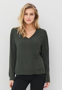 Tamsiai žalia ilgomis rankovėmis palaidinė su V formos iškirpte ir priekinėmis kišenėmis, pagaminta iš lygaus audinio, turinti laisvą siluetą ir minimaliai išpuošta.