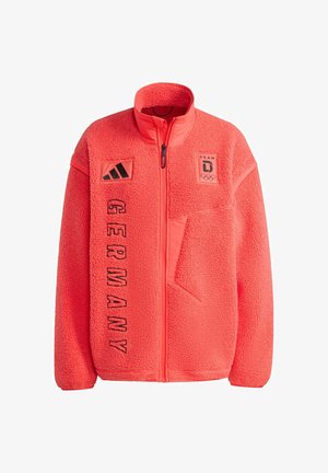 Chaqueta brillante de forro polar coral con cuello alto, cierre de cremallera, logo del equipo en negro y texto "GERMANY" en el frente. Cuenta con bolsillo lateral.