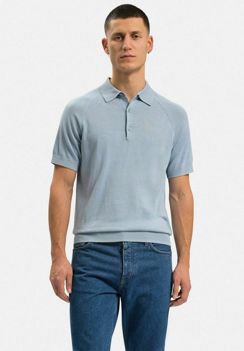 Ljust blå stickad polo-shirt med krage, korta raglanärmar och en texturerad yta, i kombination med blå denimjeans.
