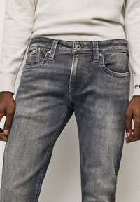 Grå denimjeans med en urtvättad finish, femfickorsdesign, bältesömmar och knappgylf. Texturerad tyg med subtila färgvariationer.