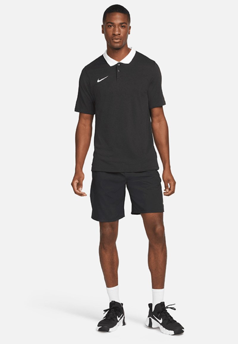 Polo noir avec col blanc, manches courtes, et logo Nike ; associé à un short noir et des baskets noires avec des accents blancs.