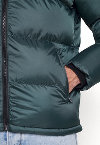 Jadegrön puffjacka med en slät, glänsande yta. Har dragkedjestängning, sidofickor och ribbade ärmmuddar. Texturerad, isolerad fabric.