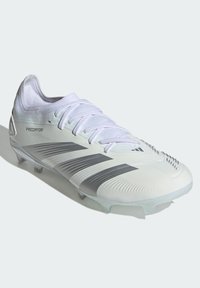 Scarpa da calcio bianca con superficie texture, caratterizzata da strisce grigie e un sistema di allacciatura frontale. Include una suola stampata con chiodi conici per la trazione.