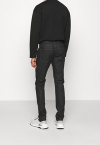 Mörkblå denimjeans med smal passform, som har bakfickor och diskreta sömnadsdetaljer. Bärs med en svart sweatshirt och vita sneakers.
