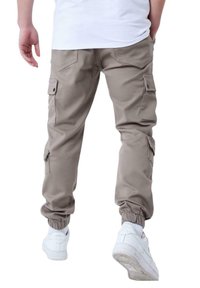 Pantalones cargo caqui con puños ajustables, múltiples bolsillos laterales y una textura de tela suave. Combinados con zapatillas deportivas blancas.