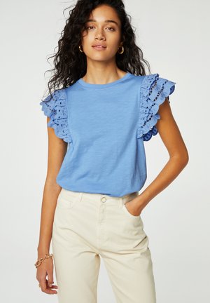 Lichtblauw t-shirt met kantafwerking aan de mouwen, met een ronde halslijn en een zachte textuur. Gecombineerd met crèmekleurige broeken.