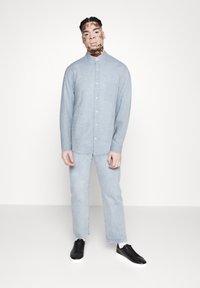 Lichtblauw overhemd met kraag, gecombineerd met lichte denim jeans en zwarte sneakers. Bevat een borstzak en heeft een soepele textuur.