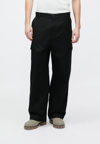 Pantaloni cargo negri cu croială lejeră, prevăzuți cu buzunare laterale, închidere cu nasture și capeți pentru curea. Țesătura are o textură netedă și durabilă.