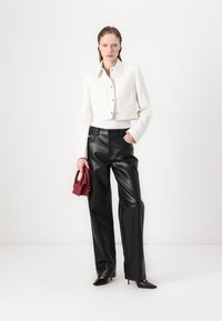 Veste blanche courte en tissu texturé avec fermeture à boutons, associée à un pantalon en simili cuir noir taille haute et un petit sac à main rouge.