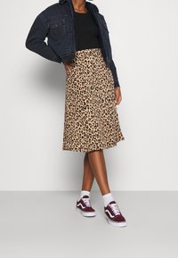 Svart topp, denimjacka med fårskinnskrag, leopardmönstrad midikjol och bordeauxfärgade sneakers med vita detaljer.