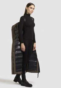 Top lungo nero a maniche lunghe e leggings abbinati a un lungo cappotto piumino con un esterno lucido nero e una fodera beige, indossato a spalla.