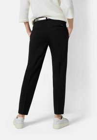 Czarne dopasowane spodnie o prostym kroju, z tylnymi kieszeniami, noszone z białymi trampkami. Gładki materiał, minimalistyczny design, bez widocznych wzorów.