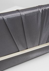 Pochette en satin gris avec un design plissé et une fine bordure en métal doré à la base sur fond blanc.