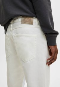 Jeans de mezclilla blanca con una etiqueta que dice "PULL&BEAR" en la parte trasera. Presenta dos bolsillos traseros y un corte recto, mostrado junto a un sudadera gris.