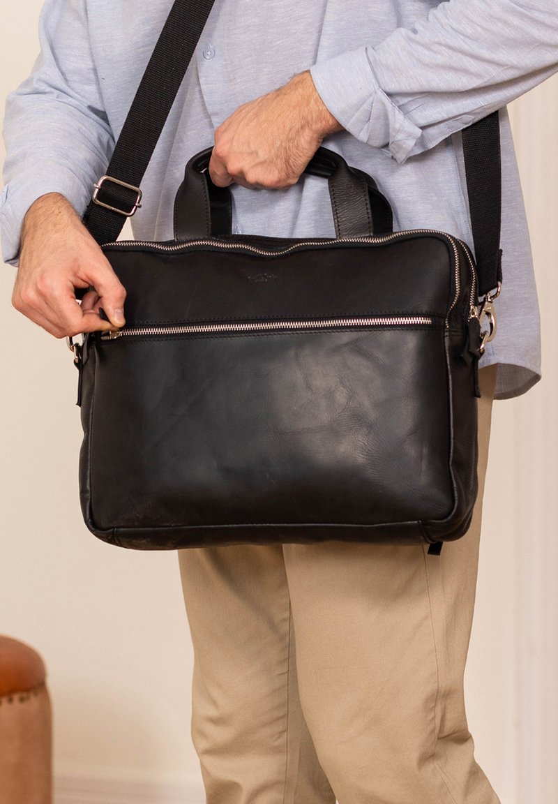 Borsa per laptop in pelle nera con doppio manico superiore, tracolla regolabile, texture liscia e tasca frontale con zip. Design minimalista con accenti metallici.