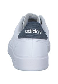 Vit atletisk sneaker med en texturerad mörkblå häl, med "adidas"-logotypen i vitt. Slät yta och förstärkta sömdetaljer.