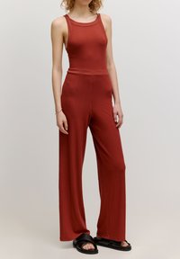Geribbelde, roestkleurige jumpsuit met een aansluitende bovenkant en wijde broekspijpen, voorzien van een ronde hals en een gladde, zachte textuur.