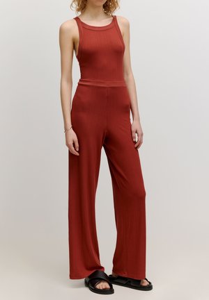 Geribbelde, roestkleurige jumpsuit met een aansluitende bovenkant en wijde broekspijpen, voorzien van een ronde hals en een gladde, zachte textuur.