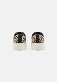 Zapatillas con parte superior de tejido beige que presenta un patrón de manchas negras, con una pestaña en el talón negra y una suela de goma blanca con una superficie texturizada.