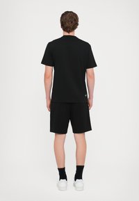 Černé tričko s krátkým rukávem a černé šortky zobrazené zezadu, mají jednoduchý design a štítek s logem u lemu.