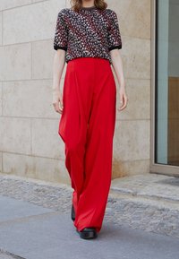 Rote weit geschnittene Hosen, kombiniert mit einem kurzärmeligen schwarzen Oberteil mit floralen Mustern. Glatter Stoff, lockerer Schnitt, einfarbig und mit kontrastierenden Besätzen.