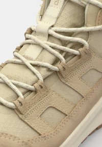 Beige High-Top Sneaker mit einer strukturierten Oberseite mit dezenten Mustern, verstärkten Ösen und runden Schnürsenkeln. Leichte Gummisohle.