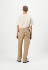 Beige cargo pants with multiple pockets and a label at the back. The top is a light-colored, short-sleeved shirt. Minimalist design.