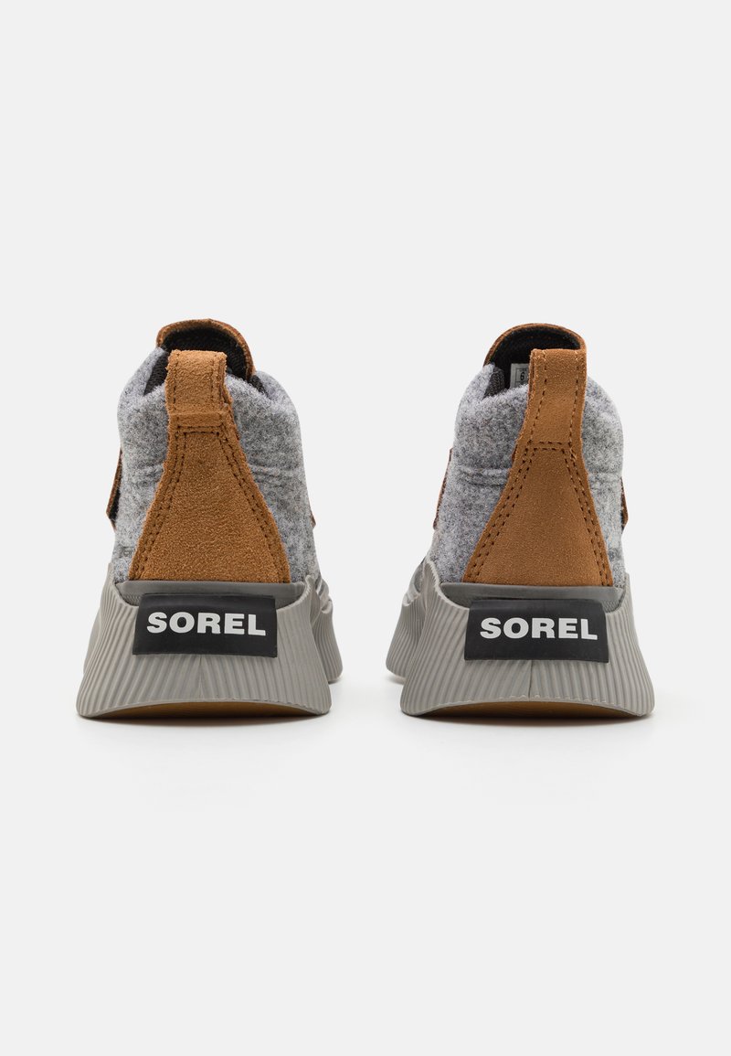 Baskets grises avec une tige en laine et en daim, accents marron et semelle grise nervurée. Logo "SOREL" visible à l'arrière. Anses pour un enfilage facile.