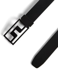 Svart bälte med strukturerad tyg, rektangulär svart metallspänne med en vinklad logotypdesign. Slät avsmalnande ände.