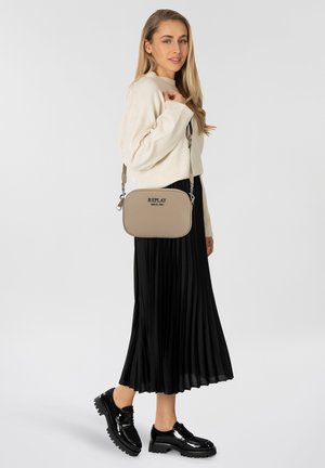 Beige schoudertas met een gladde textuur, voorzien van een bovenste rits en logo. Gepaard met een beige gebreide trui en een zwarte geplooide rok.