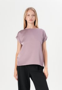 Lavender short-sleeve top with a relaxed fit and subtle sheen, featuring a round neckline and rolled sleeves, paired with black trousers.