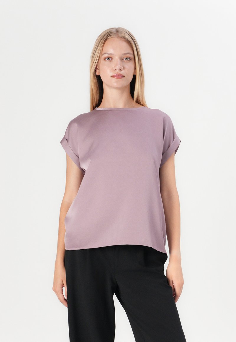 Lavender short-sleeve top with a relaxed fit and subtle sheen, featuring a round neckline and rolled sleeves, paired with black trousers.