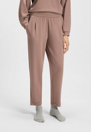 Pantaloni elastici rosa chiaro con vita elasticizzata, tasche laterali, gambe affusolate e texture morbida, abbinati a calzini grigi a coste.