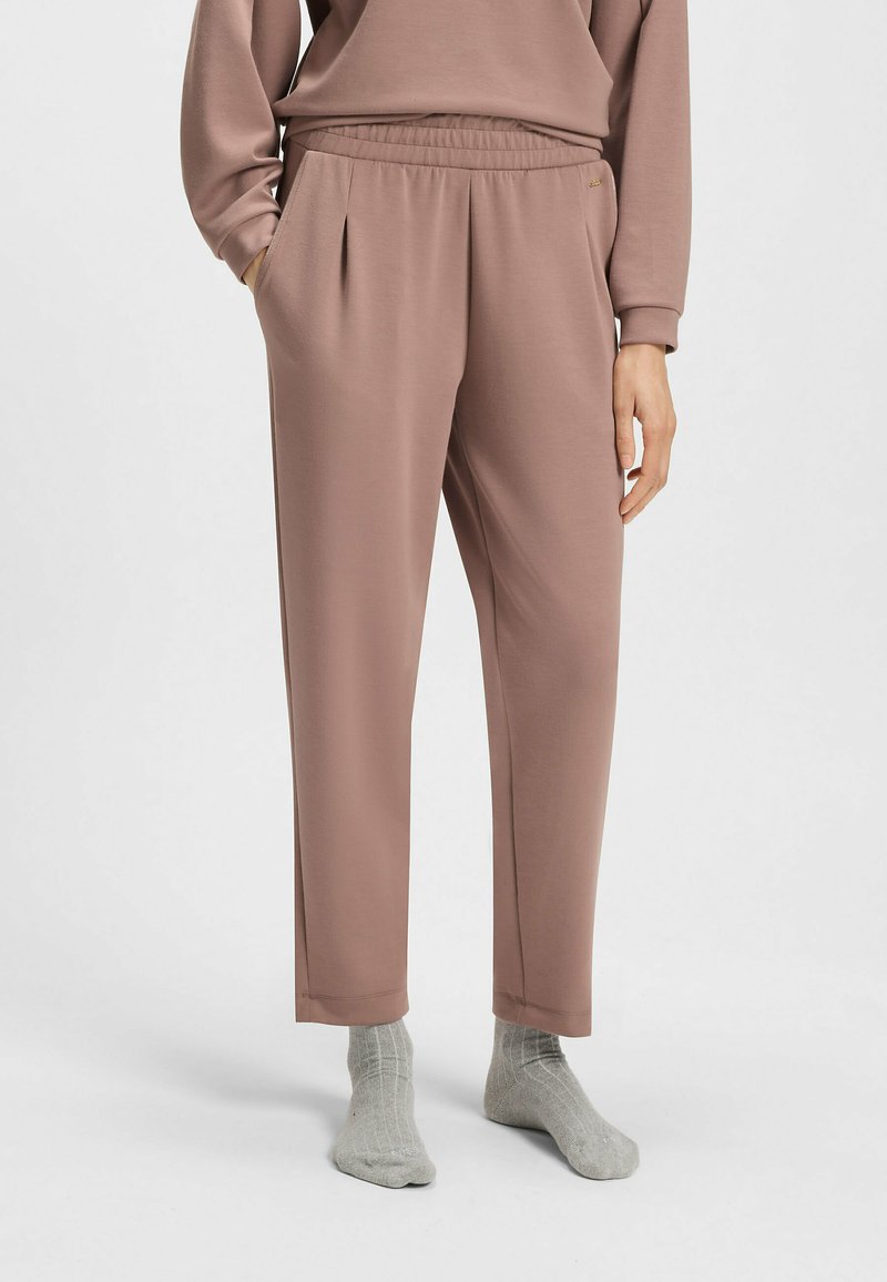 Lichtroze, elastiche broek met zijzakken, taps toelopende pijpen en een zachte textuur, gecombineerd met grijze geribde sokken.