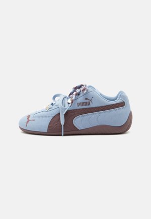Baskets Puma bleu clair avec bande latérale et semelle marron, lacets à motifs et logo Puma sur le côté et l’avant.