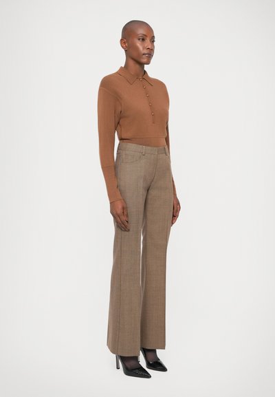 Top lung cu mânecă lungă, tricotat, de culoare maronie, cu guler și detalii cu nasturi, asortat cu pantaloni bej cu un model, cu talie înaltă și pantofi cu vârf ascuțit, negri.