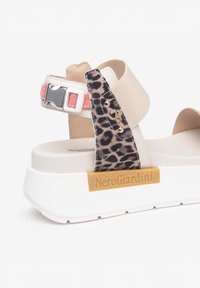 Sandale plateforme beige et imprimé léopard avec une semelle blanche, des accents roses et des détails en or, étiquetée "NeroGiardini."