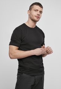 Fekete pamut póló rövid ujjakkal, kerek nyakkivág�ással, slim fit fazonnal, sötét cargo nadrággal viselve. Nincsenek látható minták vagy kiegészítők.