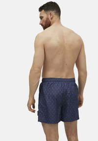 Bañador azul marino con un patrón sutil, cinturilla elástica y bolsillos laterales. El material parece ligero y suave.